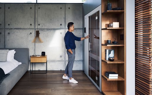 Mann vor moderner, integrierter S1 Sauna in einem offen gestalteten Schlafzimmer mit Designmöbeln.